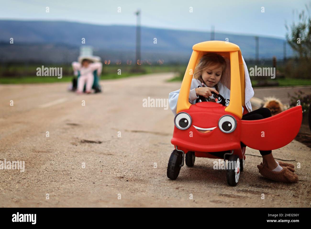 Little adorable toddler girl driving big vintage toy car and having fun with playing outdoors Stock Photo