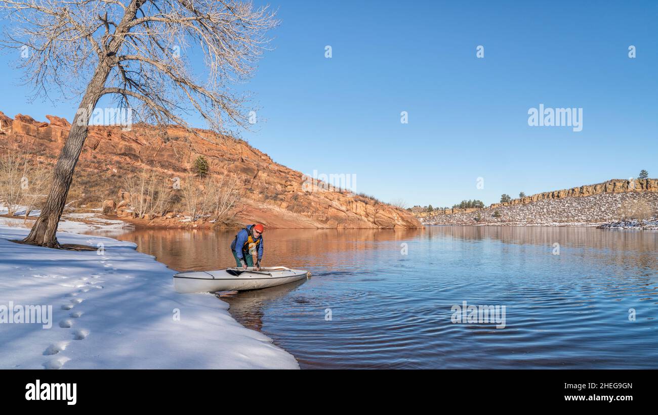 senior male wearing life jacket is paddling expedition canoe in winter