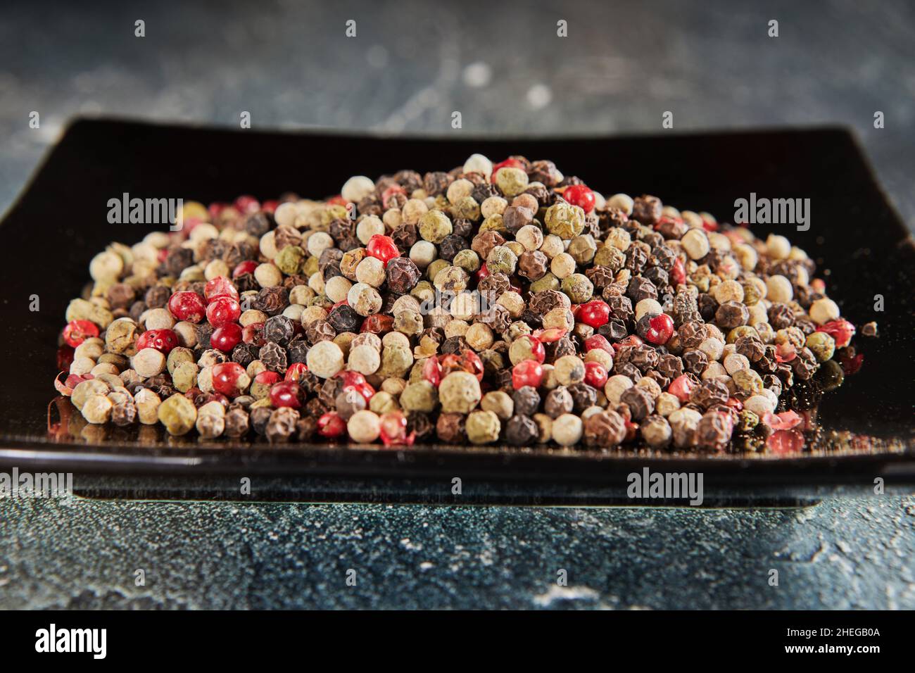 Multi-colored peppercorns on black plate with reflection Stock Photo