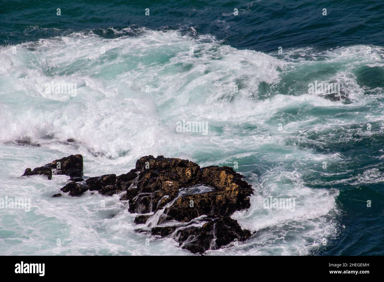 Foamy water forms in the ocean as waves break over the rocks Stock