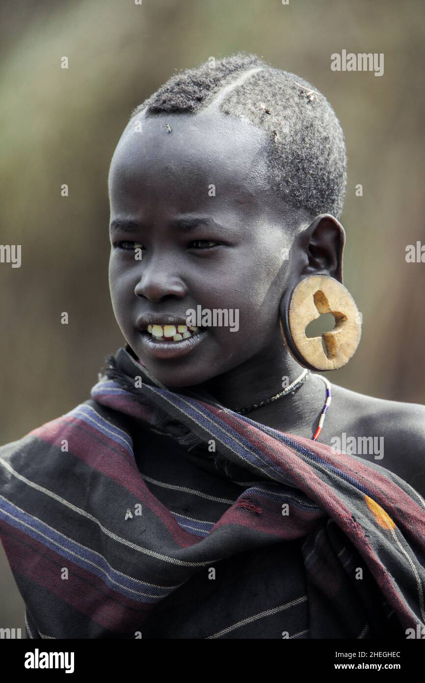 Omo River Valley, Ethiopia - November 29, 2020: Portrait of African Teenager with a big traditional wooden earrings in the local Mursi tribe village Stock Photo