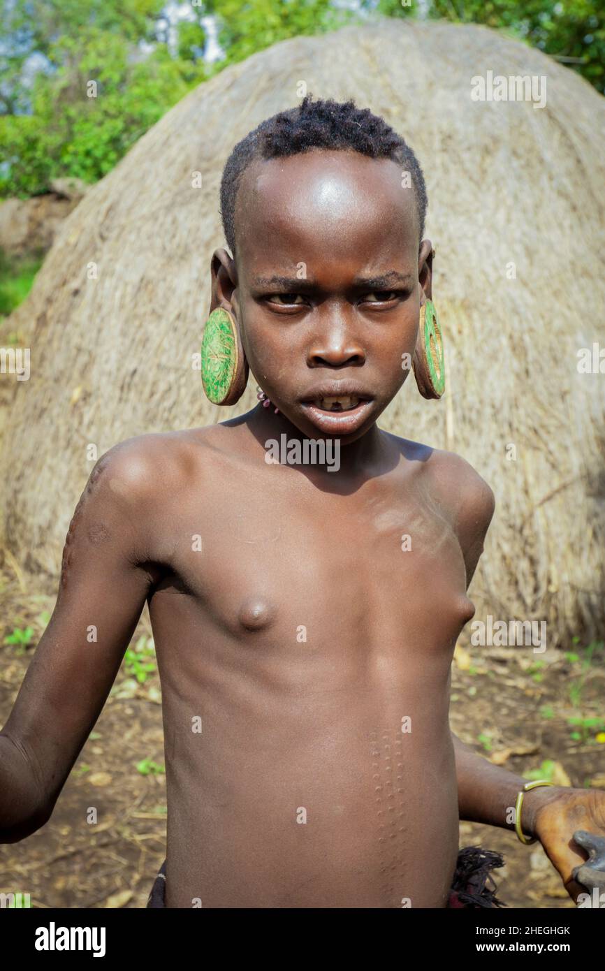 Omo River Valley, Ethiopia - November 29, 2020: Portrait of African Teenager with a big traditional wooden earrings in the local Mursi tribe village Stock Photo