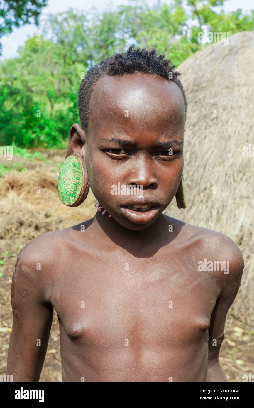 Omo River Valley, Ethiopia - November 29, 2020: Portrait of African Teenager with a big traditional wooden earrings in the local Mursi tribe village Stock Photo