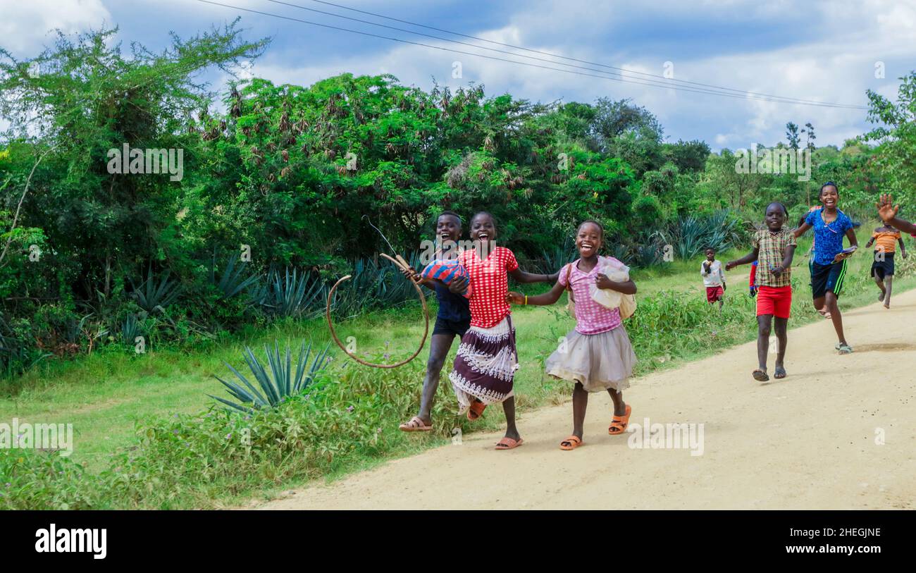 Jinka, Ethiopia - November 30, 2020: Several Smiling African Children in Bright Clothes Running on the Rural Road Stock Photo