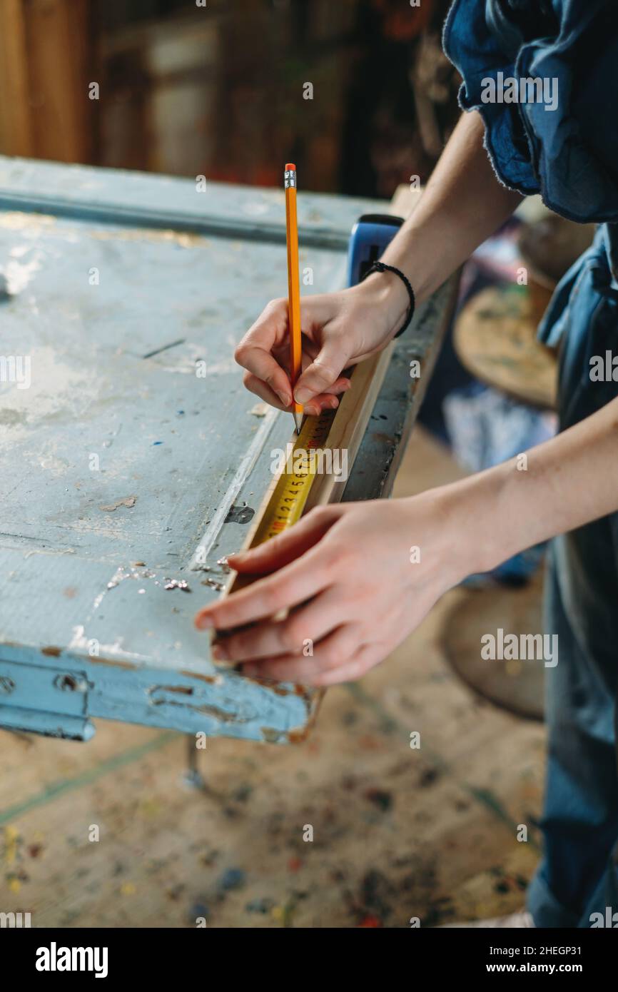 Close up view of hardworking professional carpenter woman hands working with ruler, making marks on wood. Reuse, reduce, recycle old things. Aware Stock Photo