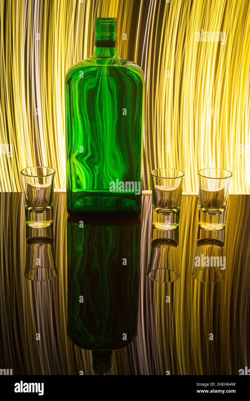 A green bottle with three shot glasses on the background which is illuminated with light painting. Stock Photo