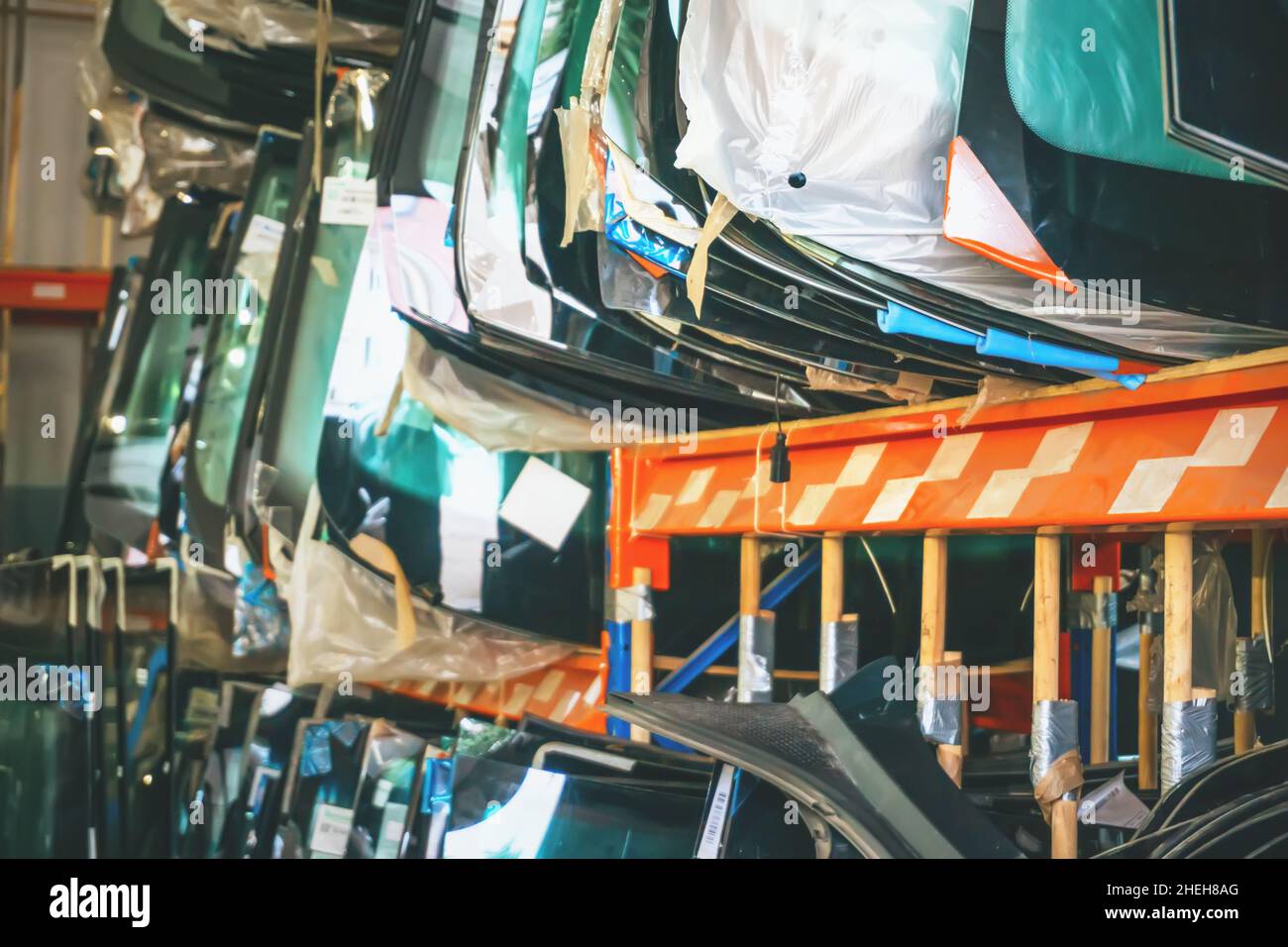 Many windshields for cars on service station shelves ready to install or replace broken glass with cars. Stock Photo