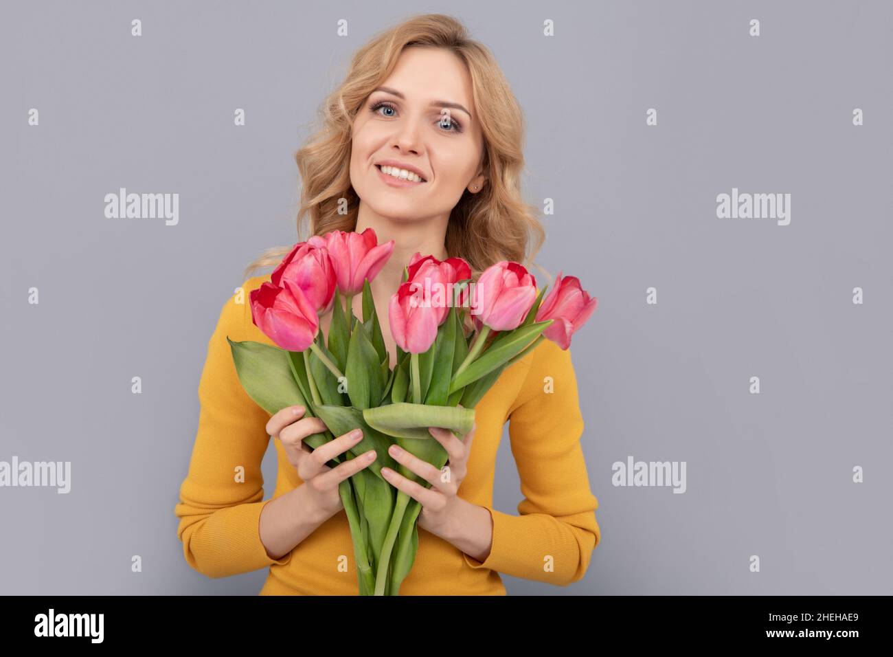 smiling girl hold flowers for spring holiday on grey background Stock Photo