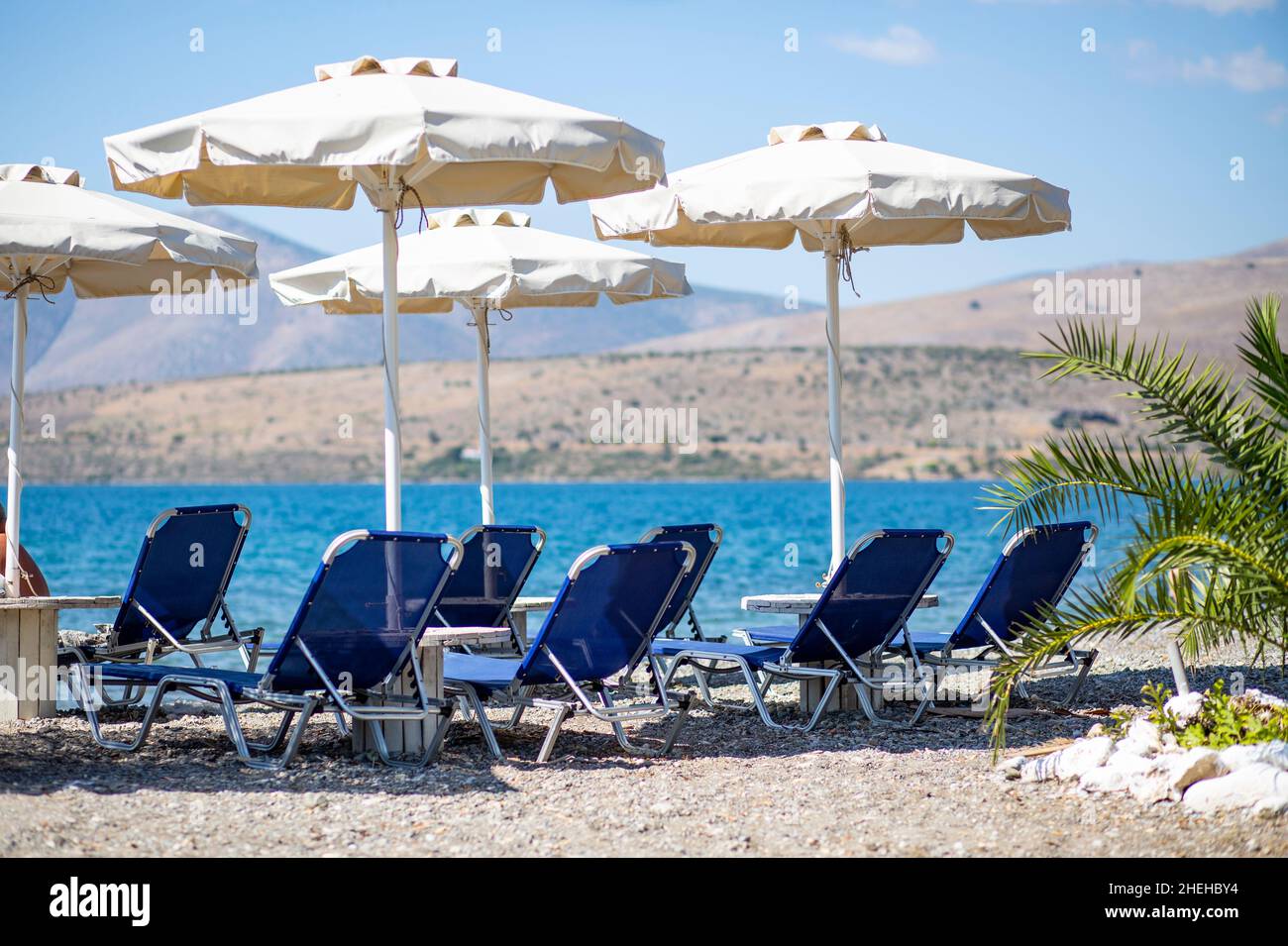 sunbeds and umbrellas abandoned on sunny beach blue sea blue sky no people Stock Photo