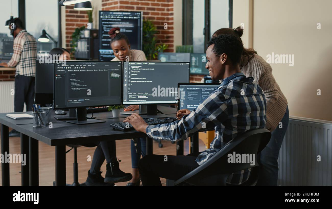 Software developer looking at running code on multiple screens takes off glasses and doing high five hand gesture with colleague programer. Programmers celebrating successful online cloud computing. Stock Photo