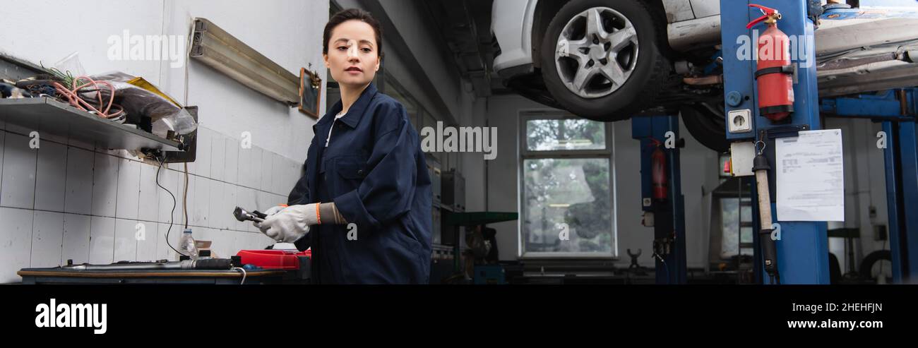 Young forewoman holding tool near car in service, banner Stock Photo