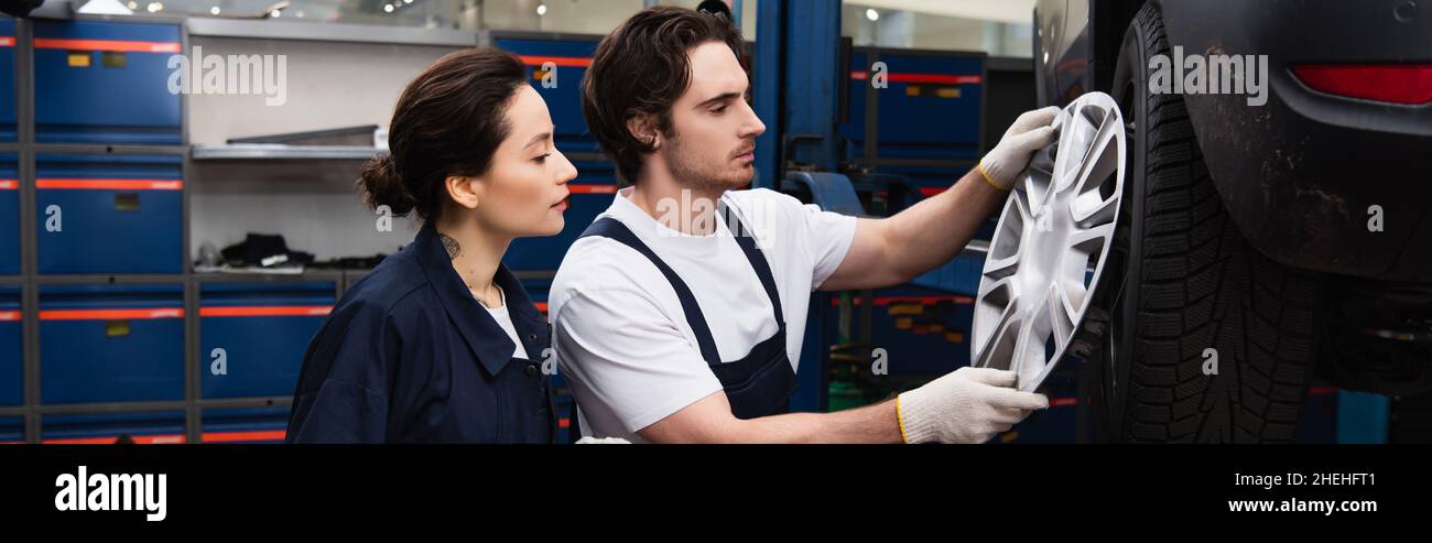 Side view of mechanics looking at wheel dink in car service, banner Stock Photo
