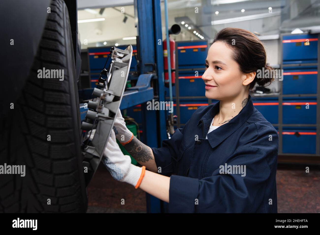 Smiling mechanic in gloves holding disk of car wheel in service Stock