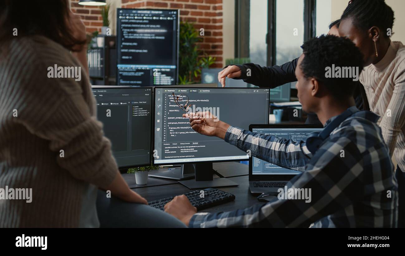 Software developers discussing about source code compiling discovers errors and asks the rest of the team for explanations in front of multiple screens running algorithms. Programmers doing teamwork. Stock Photo