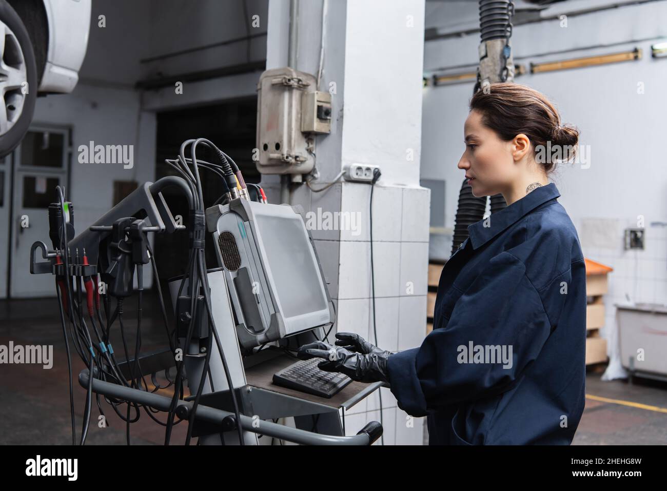 Side view of forewoman using computer near blurred car in garage Stock Photo