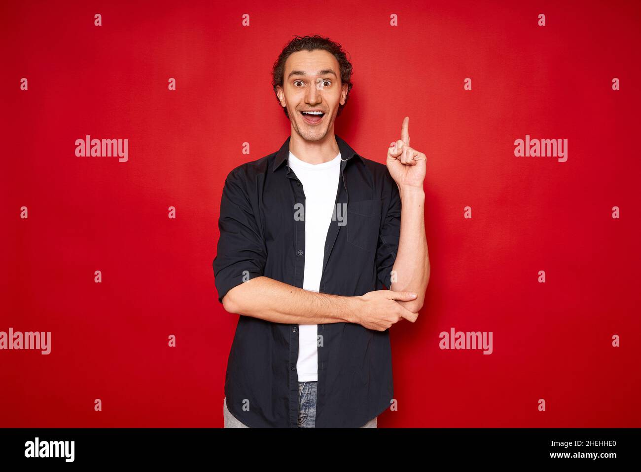 excited man points index finger up, rejoices in new brilliant idea. isolated on red background Stock Photo