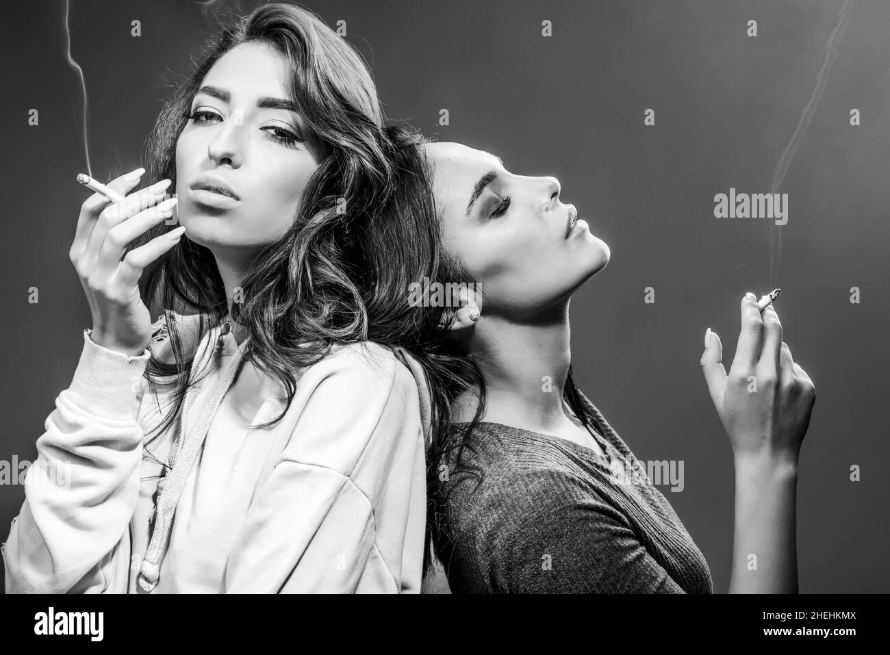 Smoking addiction. Actual social problem. Drug addict or medical abuse concept. Two sad woman with depression Smoking on the gray Background. Stock Photo