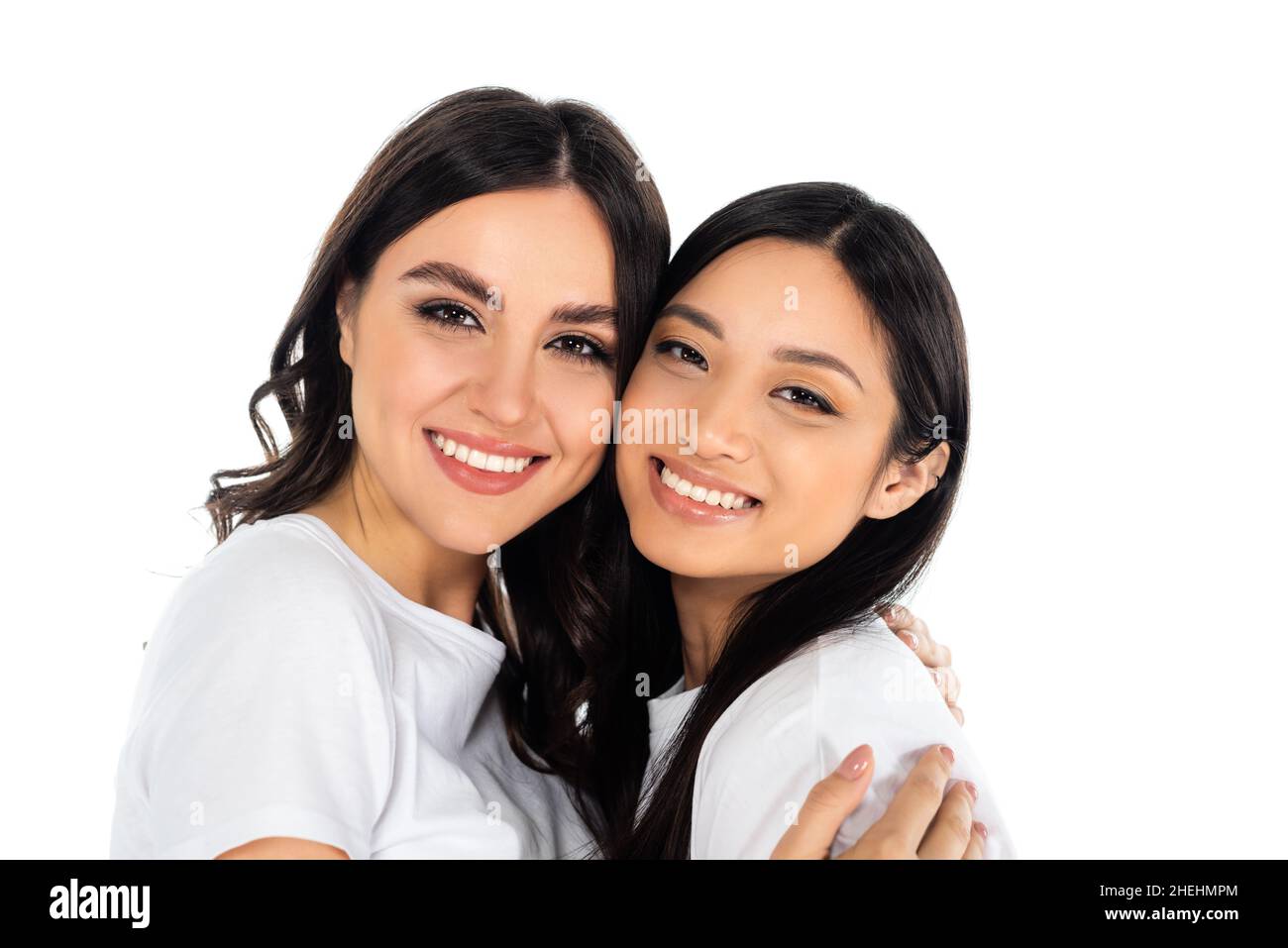 happy brunette woman embracing and looking at camera with asian friend ...