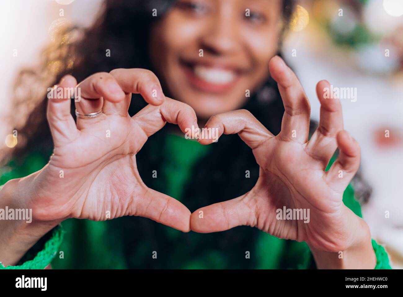 Brunette long-haired daughter and African American mother sit and pose showing hearts with fingers against Christmas decorations Stock Photo