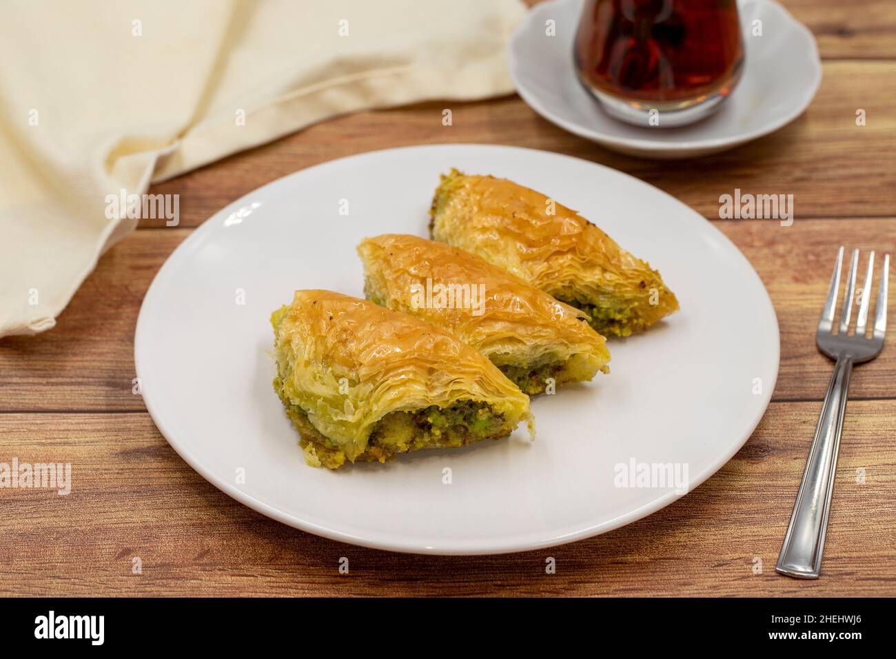 Pistachio baklava (Sobiyet) on wooden background. Traditional Turkish cuisine delicacies. Close-up. Stock Photo