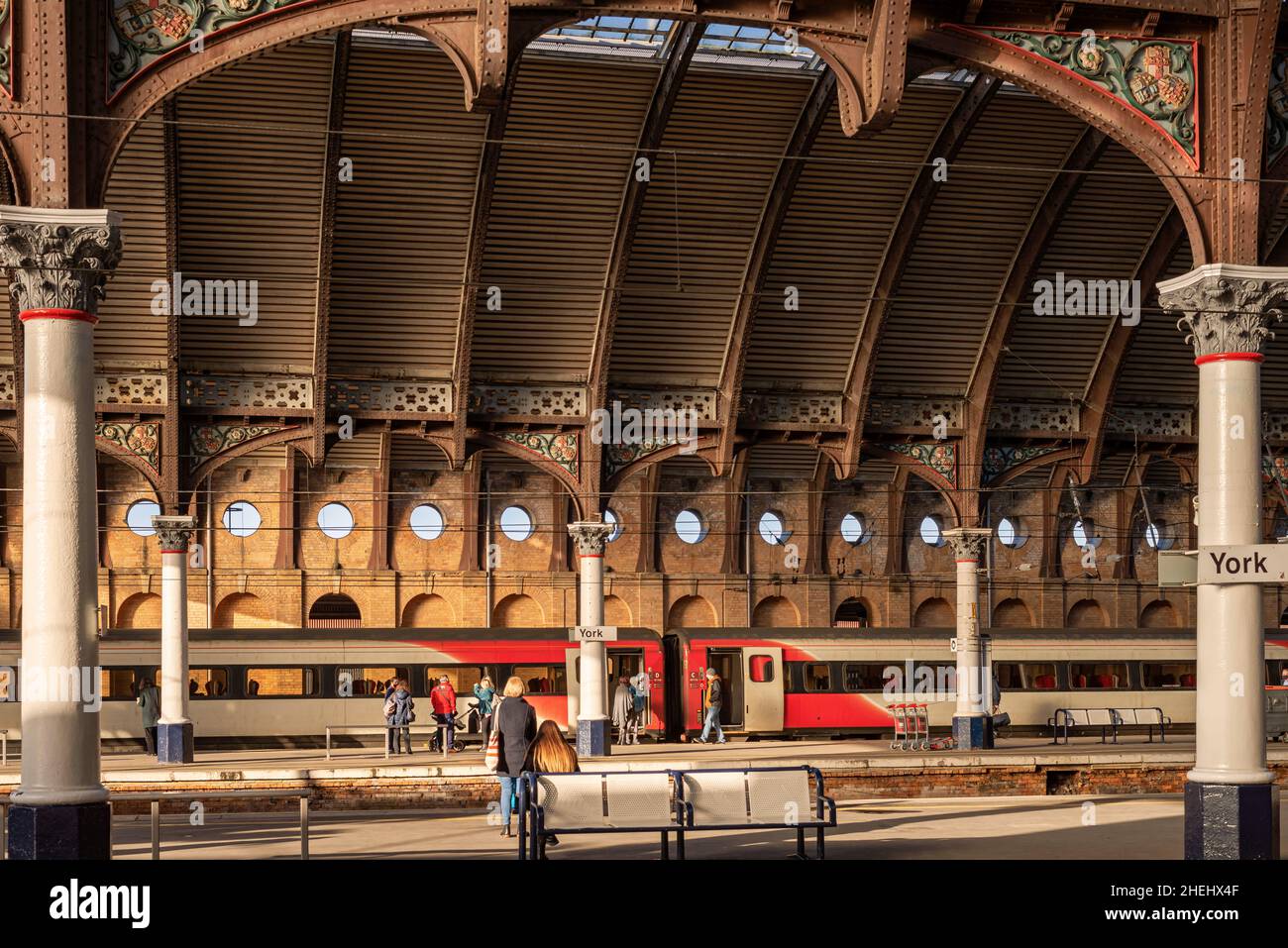 Railway station platforms with passengers waiting for a train.  Overhead is an historic canopy with columns on each side. Stock Photo