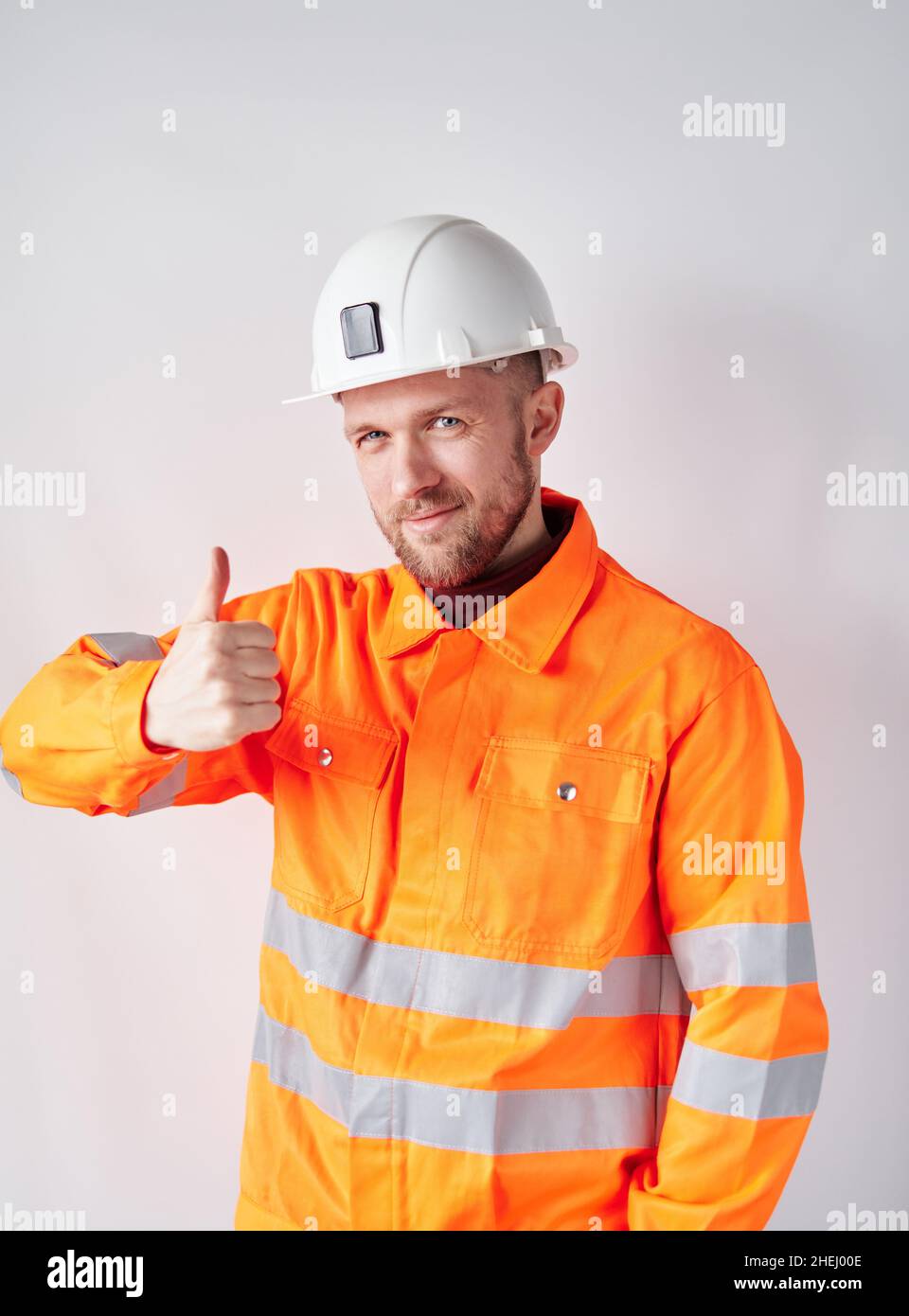 Cute caucasian chief technician, supervisor or construction architect with beard wearing worker uniform and hardhat making thumb up gesture. Construction industry concept. High quality photo Stock Photo