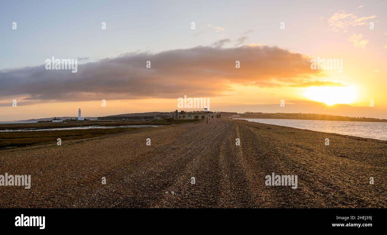 Pebble spit at sunrise leading to Hurst Castle English heritage military fort and Hurst Point Lighthouse in the distance. Stock Photo
