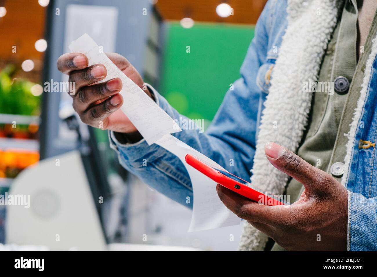 Black male person shopper checks receipt total holding smartphone standing in contemporary supermarket hall extreme close view Stock Photo