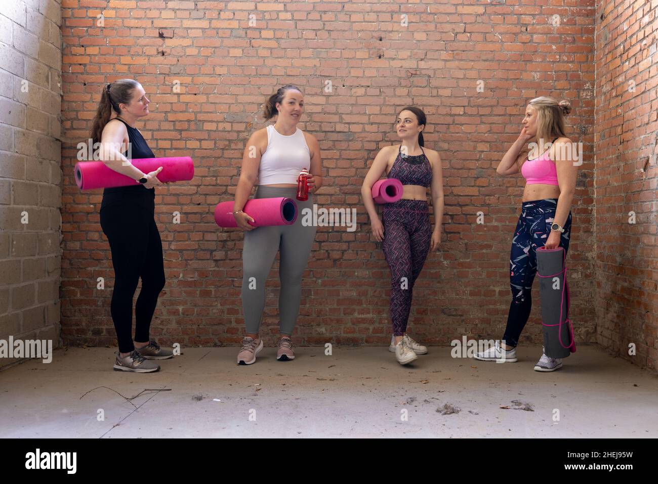 Group of young attractive sporty women of different body shapes gathered together and talking while waiting in the gym. Industrial brick wall background. High quality photo Stock Photo