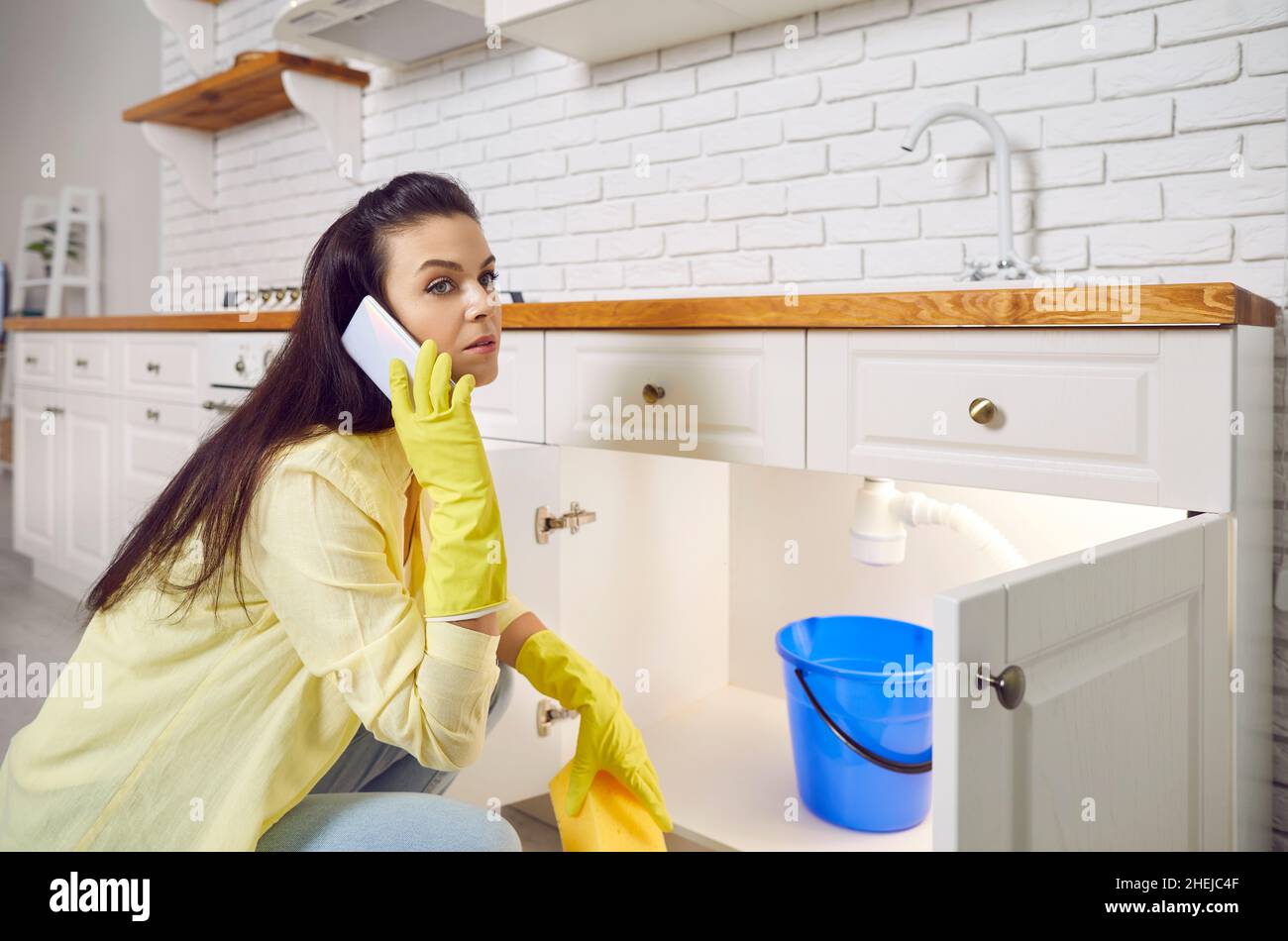 Young woman calls the plumber as she has water leaking from her kitchen