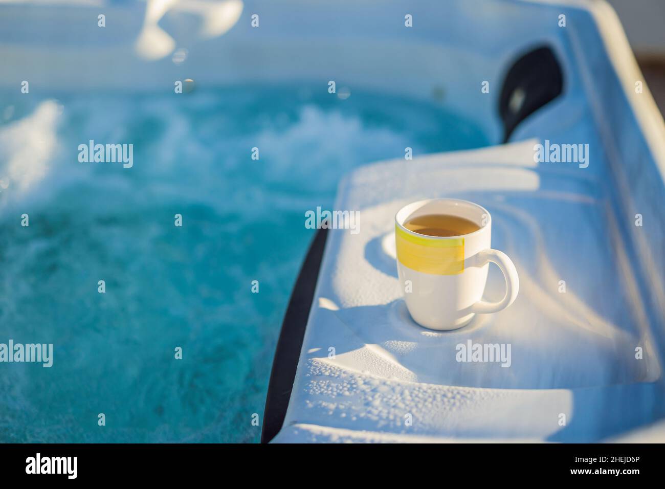 Mug with morning drink on the side of Hot tub hydromassage pool. Illuminated pool. Rest outside the city. Cottage with hydromassage pool Stock Photo