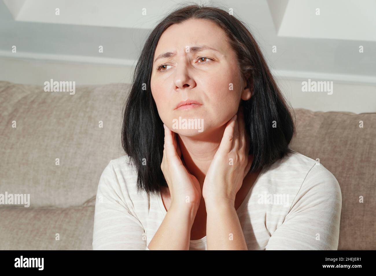Mature woman touching her neck. Sick woman feels sore throat, painful cough, pharyngitis and hoarseness. Thyroid disorder. Medical and health care. Stock Photo