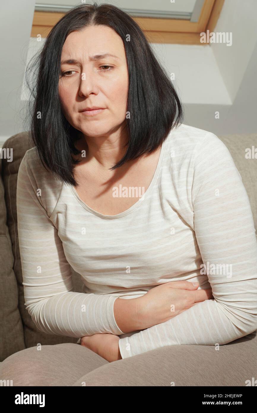 Middle aged mature woman suffering from stomach ache at home. Abdominal