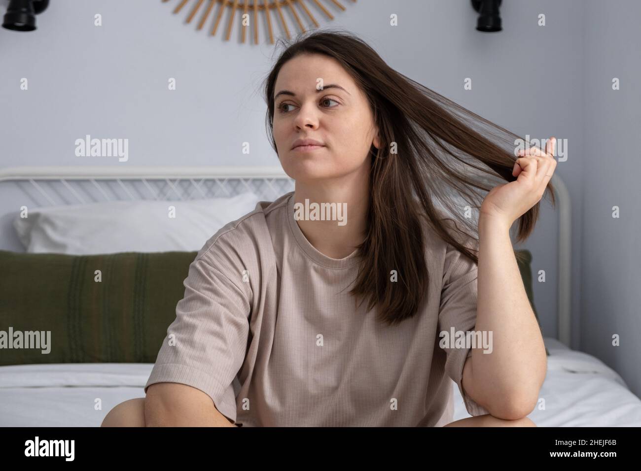Young woman sitting on bed at home. Attractive woman calming down before sleep Stock Photo