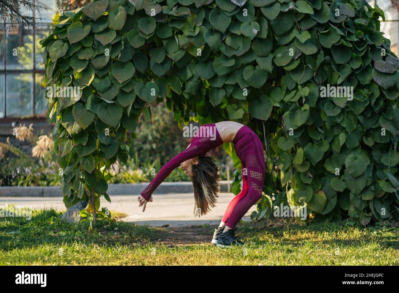 Girl in red sportswear doing yoga pose on the alley in the autumn park