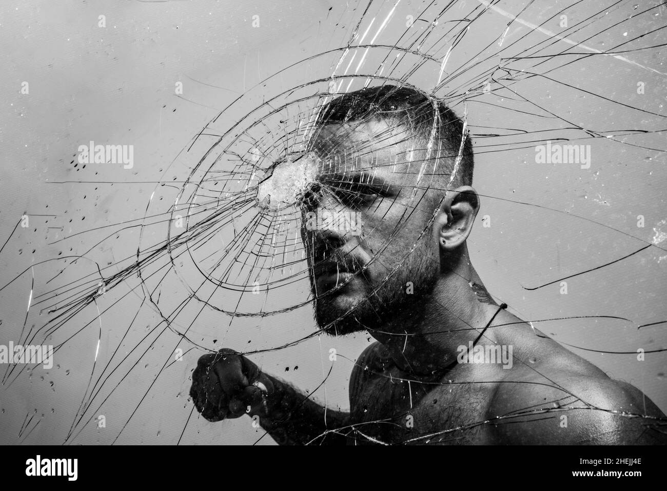 Determination to succeed. Muscular man having inner determination and commitment to break glass wall. Determined latino man removing obstacle with Stock Photo