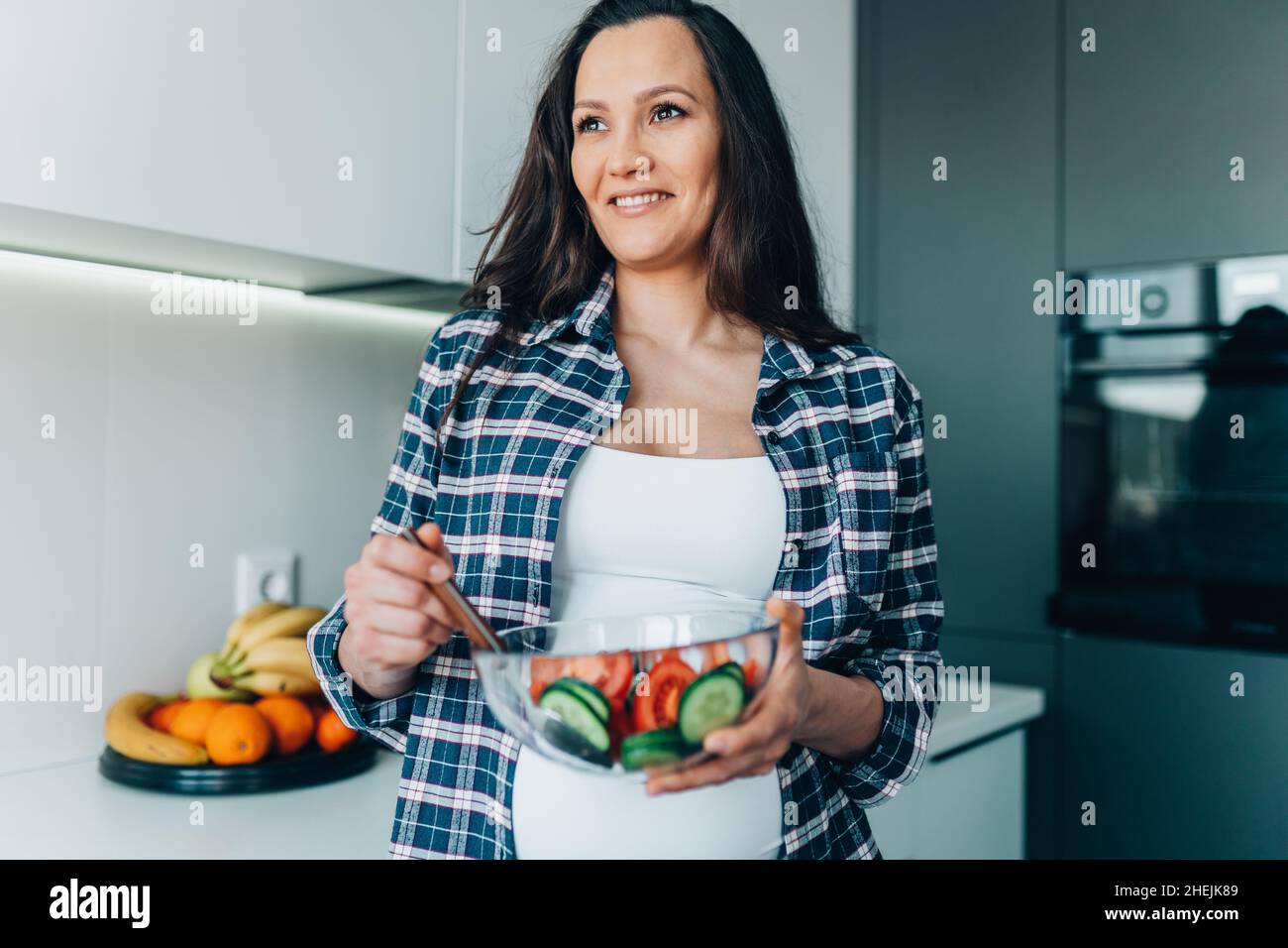 Portrait of young smiling pregnant woman mix vegetable salad with