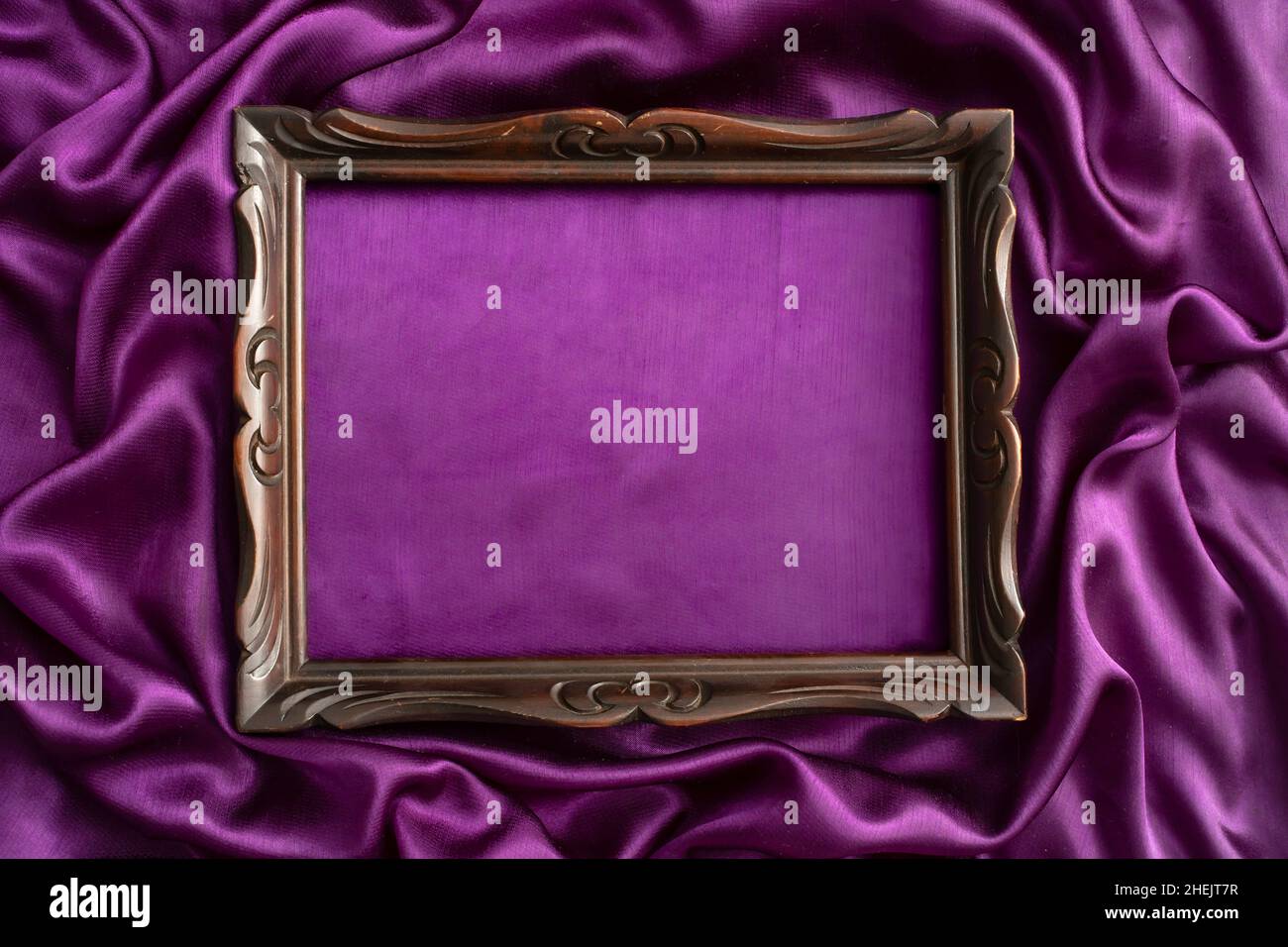 moody mockup photography, of an old sculpted wooden frame, on purple satin background Stock Photo