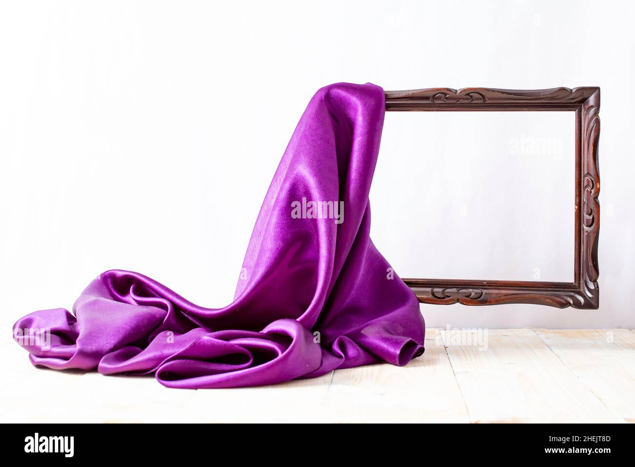 Purple satin fabric unveiling a levitating wooden empty frame, on white background Stock Photo