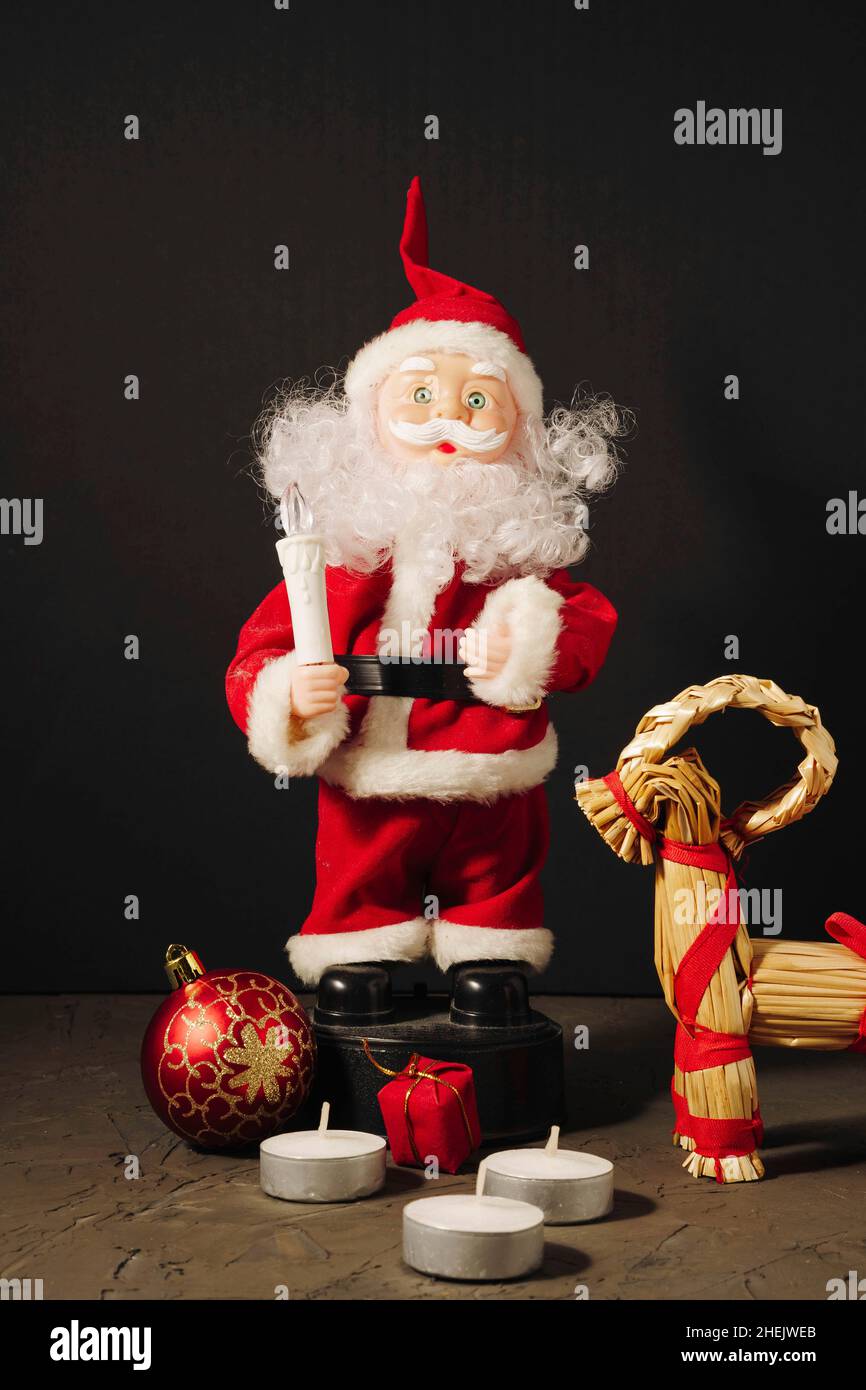 Santa Claus doll in a red suit with a candle, gifts, a Christmas ball and a Christmas deer on a dark background, Merry Christmas and New Year Stock Photo