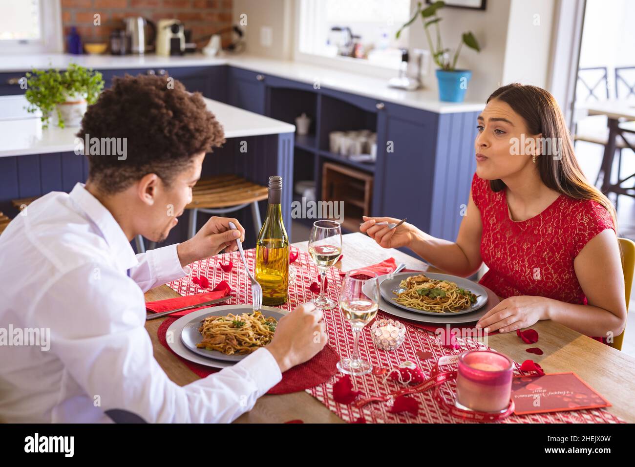Happy biracial young couple enjoying lunch date at dining table in kitchen Stock Photo