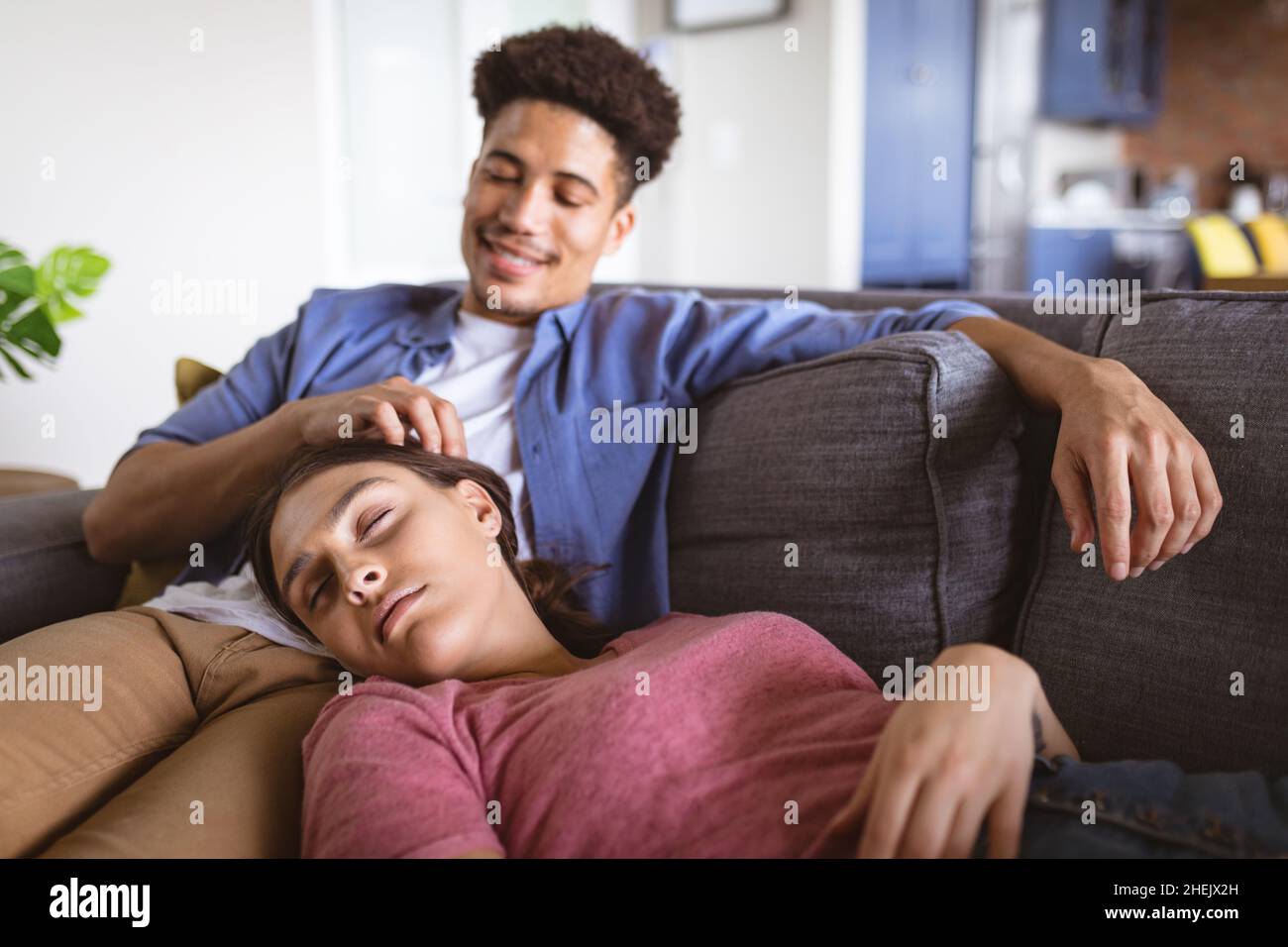 Smiling young biracial man caressing girlfriend sleeping on sofa at home Stock Photo