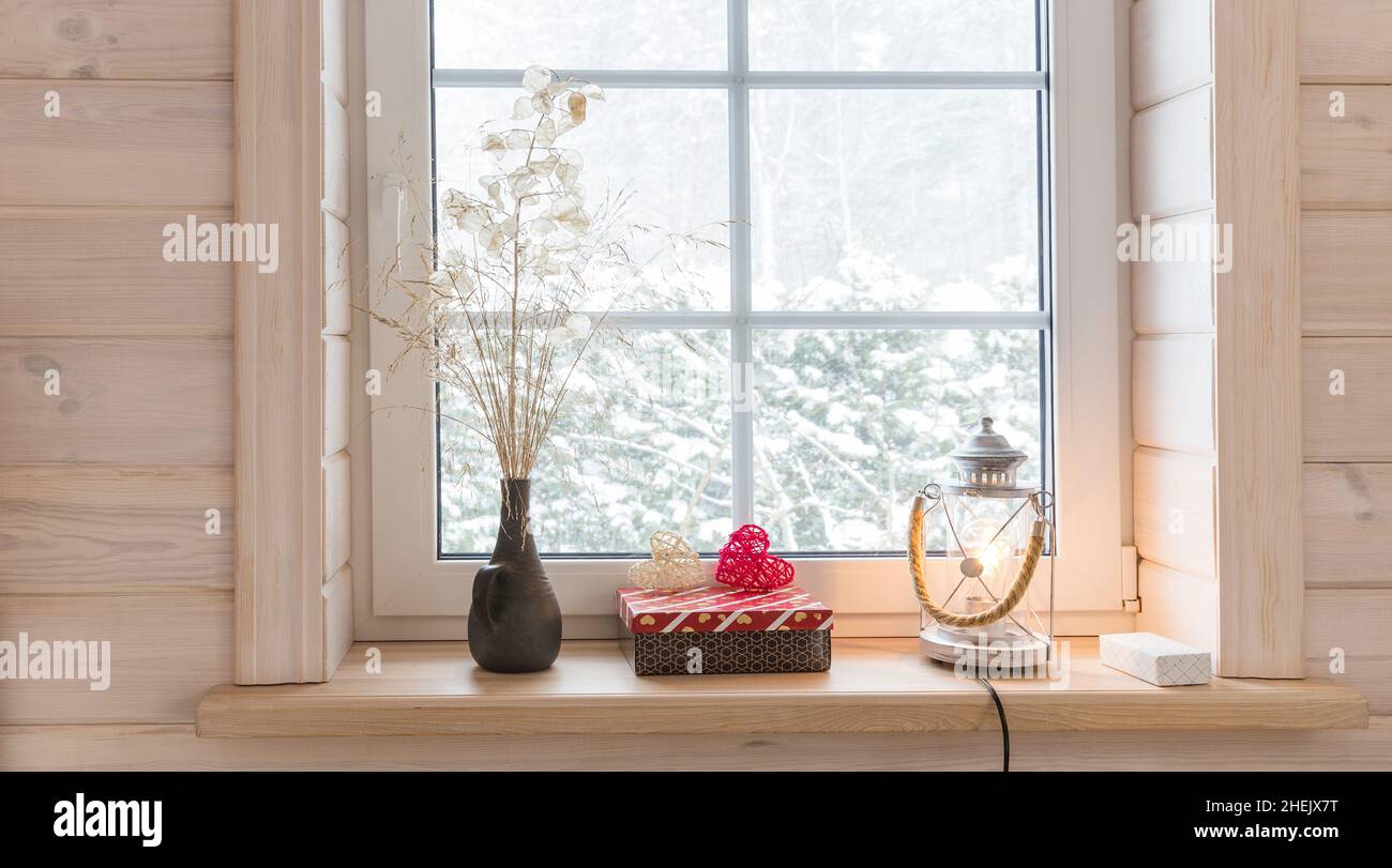 Romantic window in a white wooden house overlooking the winter garden, Scandinavian style. Lantern, candles and heart on the windowsill. Stock Photo