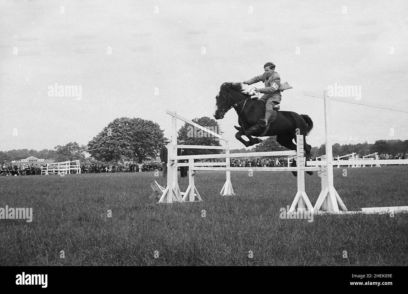 1940s, historical, outside in a field, a young boy on a horse, jumping a fence in an equestrian event at an agricultural show, no helmet, but wearing an official number or armband, England, UK. Stock Photo