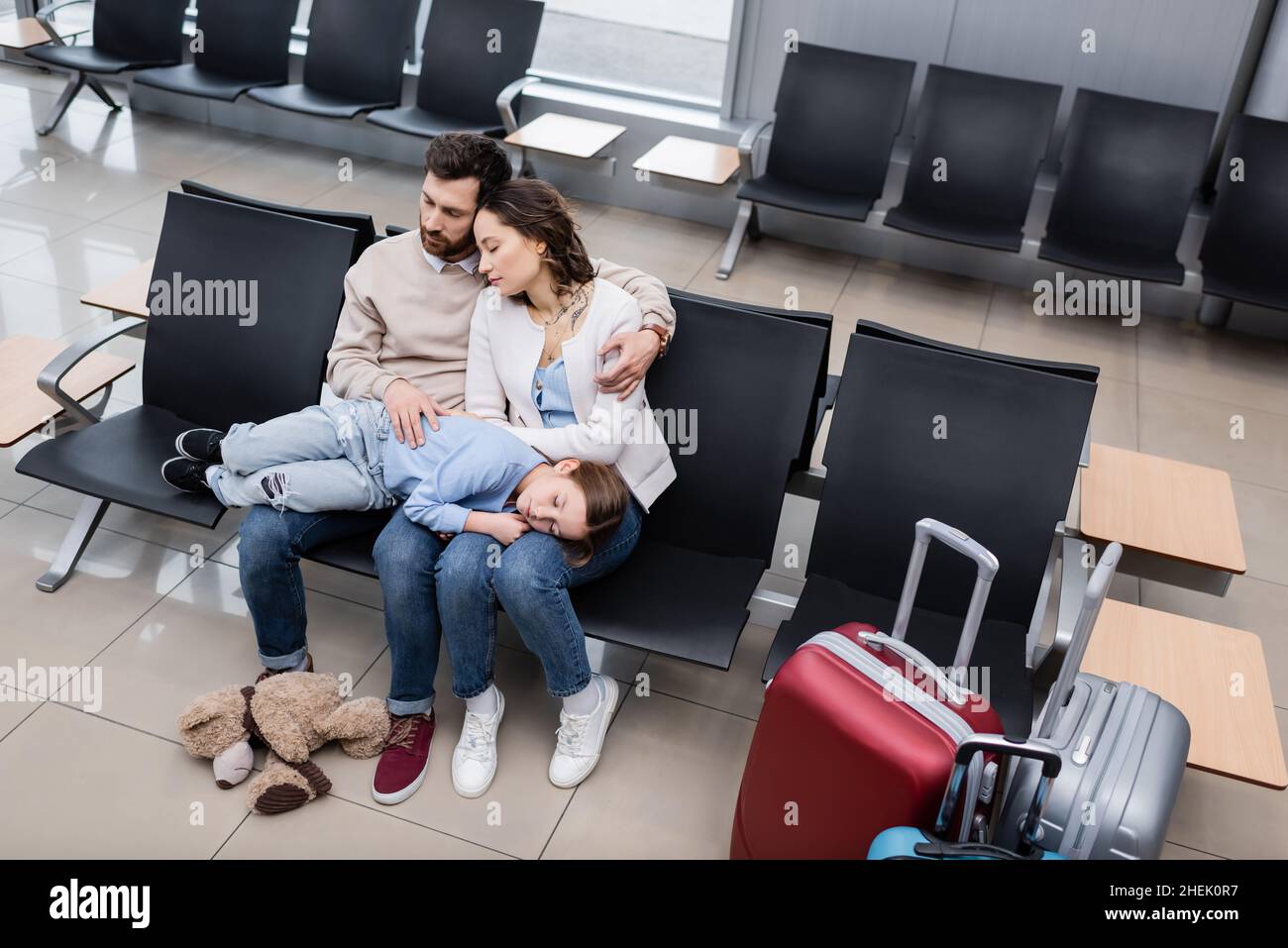 high angle view of girl sleeping on knees of tired parents in airport