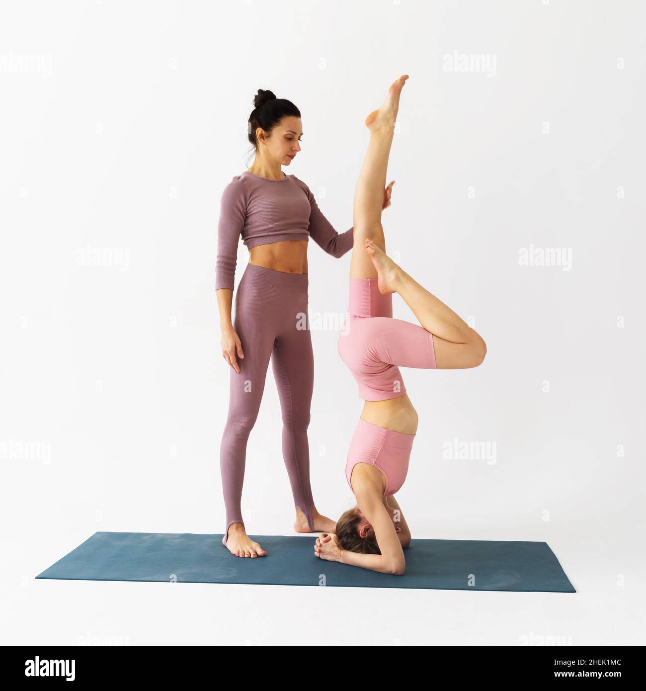 A woman trainer helps a student to correctly perform the Shirshasana exercise, an inverted asana, trains in the studio on a white background Stock Photo