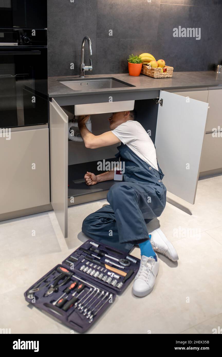 Man with tools peeking under kitchen sink Stock Photo Alamy