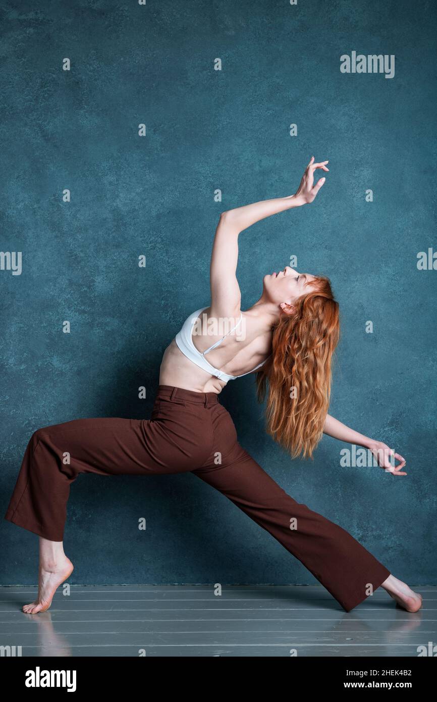 Petitie dancer with red auburn hair dancing against grey backdrop Stock Photo