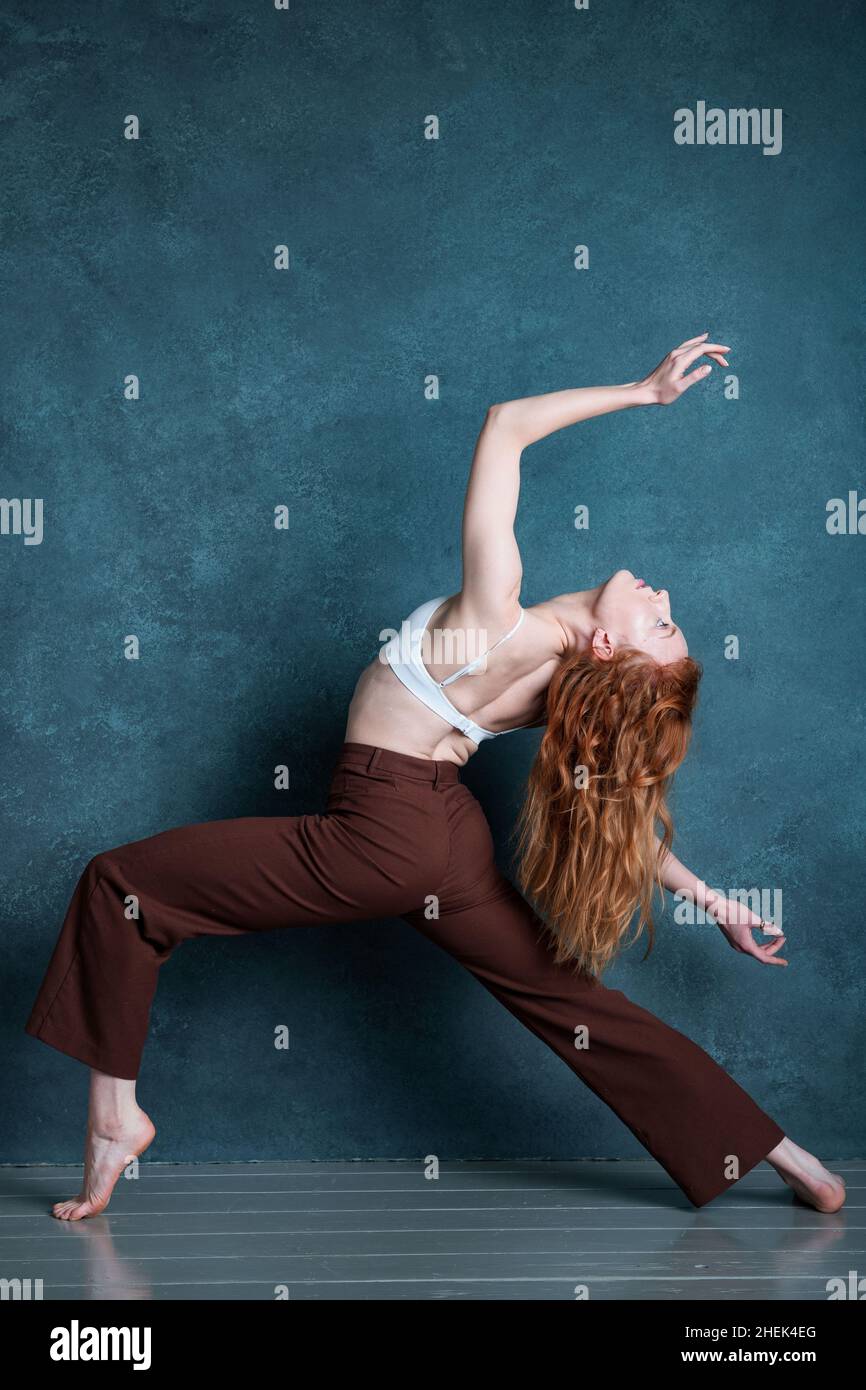 Petitie dancer with red auburn hair dancing against grey backdrop Stock Photo