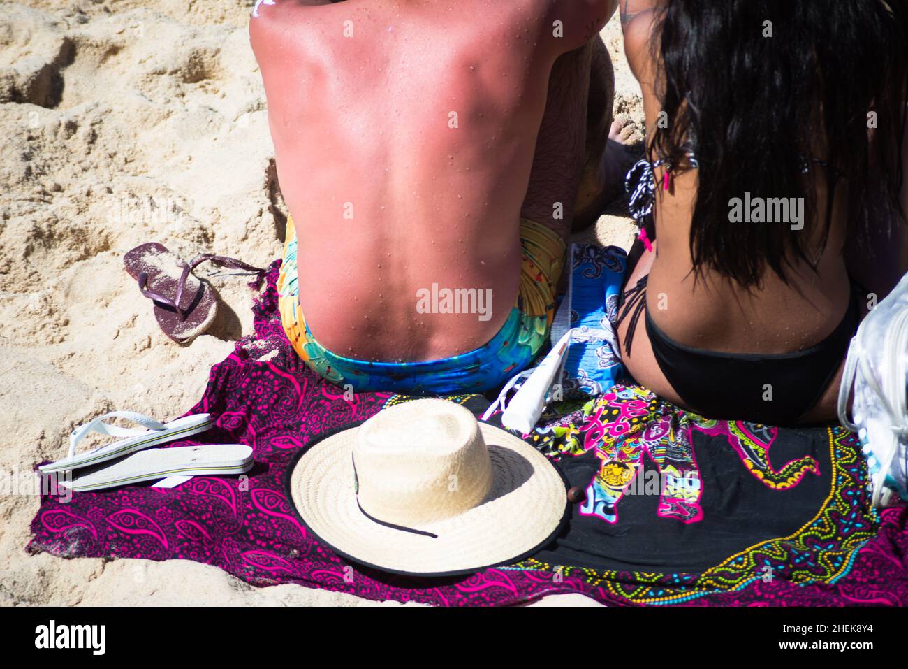 A woman and a man sitting on the sand of Farol da Barra beach in Salvador, Bahia, Brazil. Stock Photo